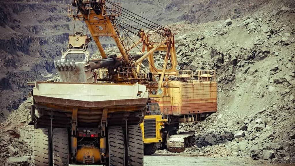 Escavadeira de mineração operando em pedreira com rochas e terra.